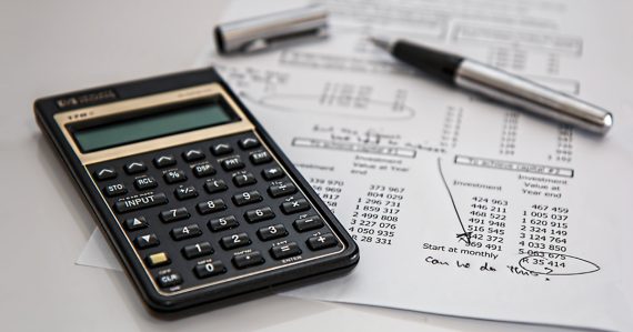 A calculator, pen and paper with figures on it.