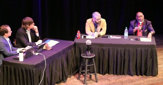 Dexter Fisher speaks into the microphone as candidate Tim Denson and moderators Russell Edwards and Drew Abney listen.